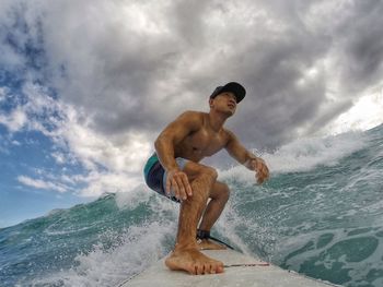 Full length of shirtless man surfing in sea against sky