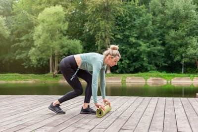 A woman in the summer in the park, unwinds a green gym mat, prepares for sports.