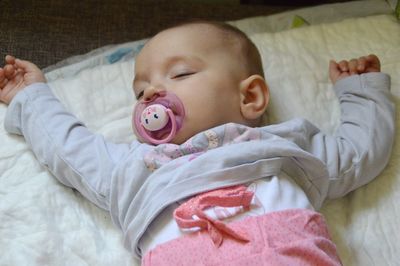 High angle view of baby with pacifier on sheet at home