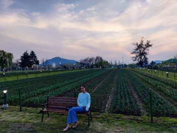 Rear view of girl  sitting on agricultural field against sky