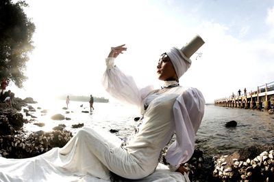 Side view of man sitting on shore against sky