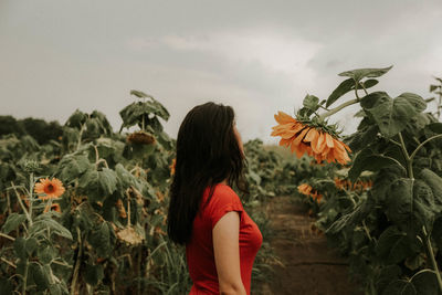 Young woman standing amidst sunflowers on field against sky