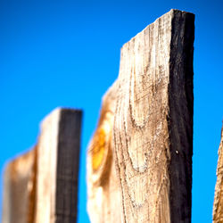 Low angle view of wooden post against clear blue sky
