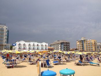 Lounge chairs at beach by buildings against cloudy sky