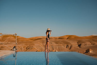 Full length of woman standing by infinity pool against sky