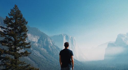 Rear view of man standing on mountain against sky