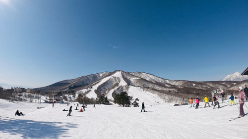 Group of people enjoying at snow covered field against blue sky