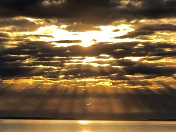 Sunlight streaming through clouds over sea during sunset