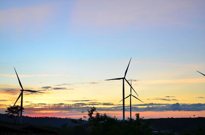 Silhouette wind turbines on landscape against sky during sunset