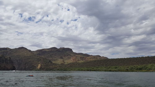 Scenic view of sea by mountain against sky