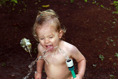 High angle view of shirtless girl drinking water from hose while standing on field