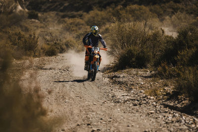 Male biker with protective sportswear riding motorcycle on dirt road