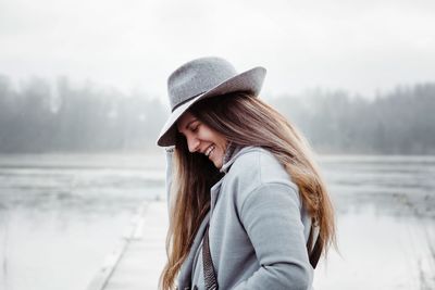 Profile of a woman with long brown hair and a hat on laughing smiling