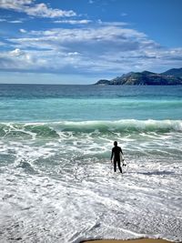 Rear view of woman walking on beach against sky