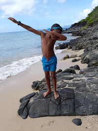 Full length of shirtless boy gesturing while standing on rocks at beach