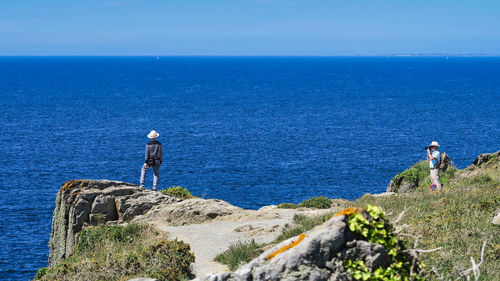 People standing on rock by sea against blue sky