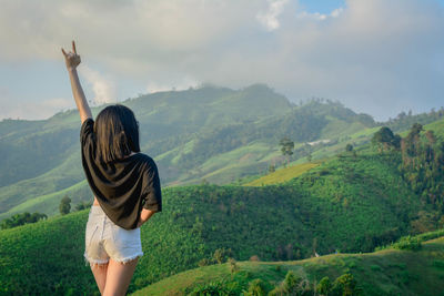 Rear view of woman standing on mountain against cloudy sky