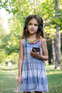 Smiling girl listening music while standing at park