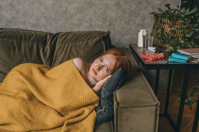 Young woman in golden blanket, peacefully sleeping on cozy couch. side table holding essentials