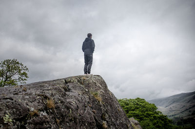 Rear view of man standing on cliff against sky