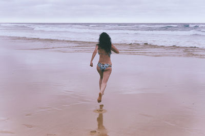 Rear view of woman running on shore at beach