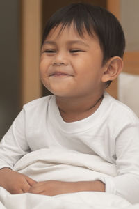 Portrait of cute boy sitting on bed at home