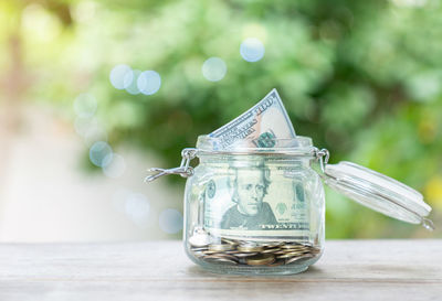 Concept of saving dollar bills and coin in glass jar on out of focus background.