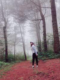 Full length of man standing by tree trunk in forest