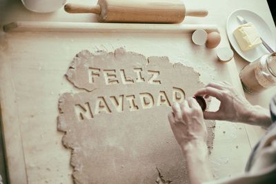 Midsection of woman using pastry cutter to cut alphabets from dough on table