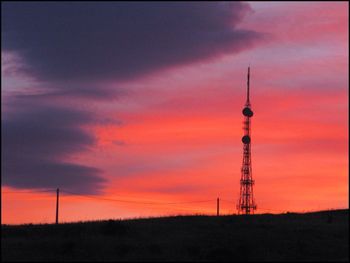 Communications tower on field against sky during sunset