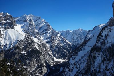 Low angle view of snowcapped mountains against clear blue sky