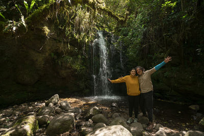 Portrait of a young couple taking photos next to a waterfall in the middle of a forest