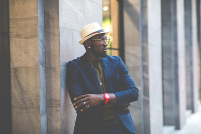 Young man looking away while standing against wall