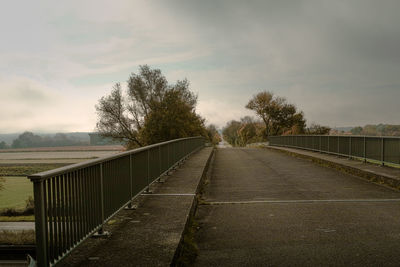 Empty road by trees against sky