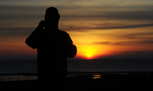 Silhouette person standing on beach against sky during sunset