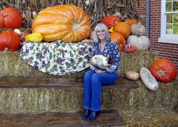 Woman with cat sitting among pumpkins on bales of straw