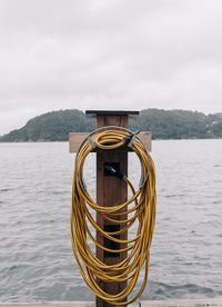Hose hanging on wooden post against lake