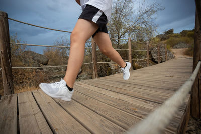 Low section of person running on wooden bridge against sky