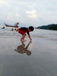 Side view of boy playing with paper boat at beach against sky