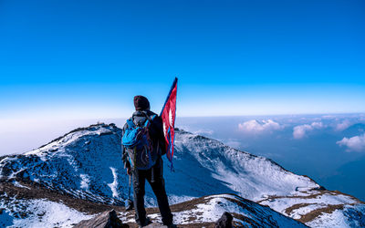 Rear view of woman standing on snowcapped mountain against clear blue sky