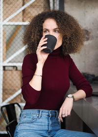 Portrait of young beautiful curly brunette woman drinking coffee while sitting at table in cafe.