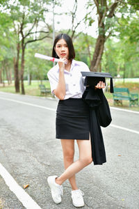 Student wearing graduation gown while standing on road at park