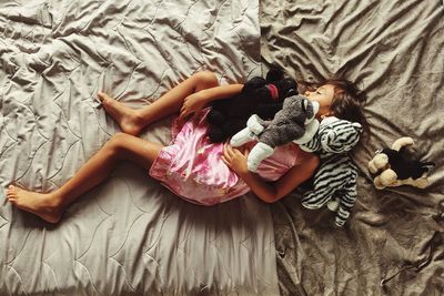 Directly above shot of girl with stuffed toys sleeping on bed at home