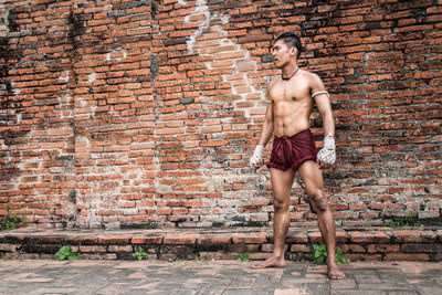 Full length of young man standing against brick wall