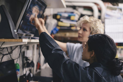 Female mechanics pointing at computer monitor while discussing in auto repair shop