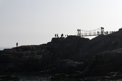 People on rock by sea against clear sky