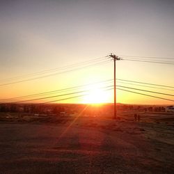 Electricity pylons on landscape at sunset