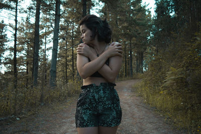 Young woman with arms crossed standing in forest