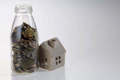 Close-up of model home and coins jar over white background
