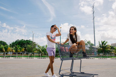 Full length of happy friends with shopping cart on parking lot